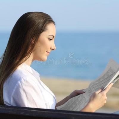 Donna che legge un giornale fuori sulla spiaggia